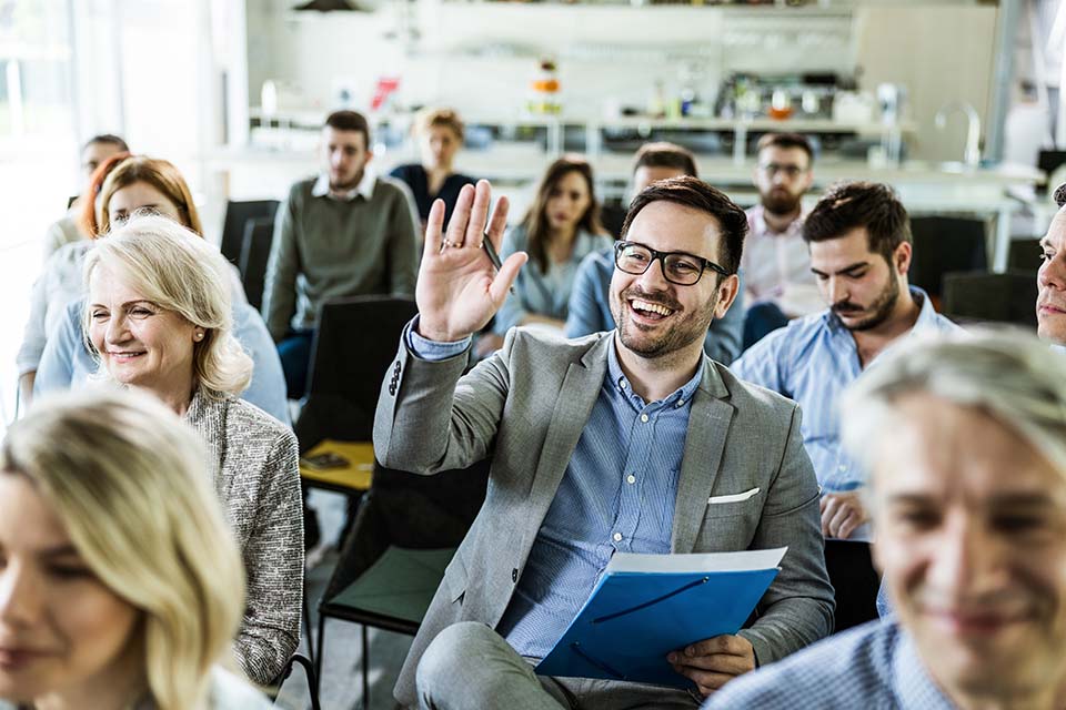 image of a happy man raising his hand to answer the question on training class in a board room.